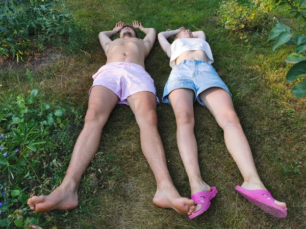 A young man in shorts and a woman in a top and shorts are lying on their backs and resting on the grass. Top view from the side of the legs.