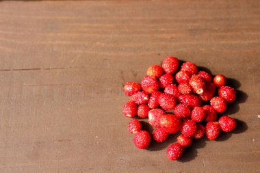 Koyu kahverengi ahşap bir masada bir avuç olgun, taze yabani çilek..