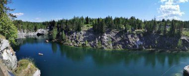 Kayalar, mağara ve turkuaz su manzaralı Panorama Ruskeala Dağ Parkı 'nda, kayıklar, gökyüzü ve ağaçlar güneşli bir yaz gününde yansıtılır..