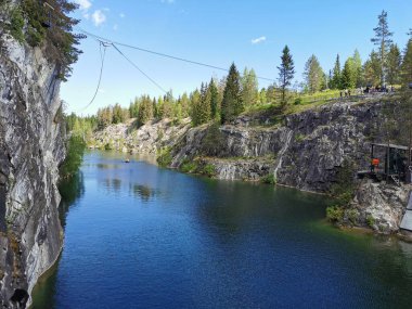 Güneşli bir yaz gününde Ruskeala Dağ Parkı 'ndaki Mermer Kanyon' un resimli kayalık kıyıları, halat ve turkuaz suyu manzarası.