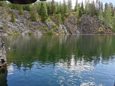 Güneşli bir yaz gününde Ruskeala dağ parkında ağaçların yetiştiği su basmış Mermer Kanyon 'un yamacındaki mağaranın manzarası..