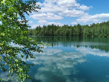 Göl kıyısında, Ruskeala dağ parkında, ağaçları ve gökyüzünü yansıtan turkuaz suyla aydınlık..