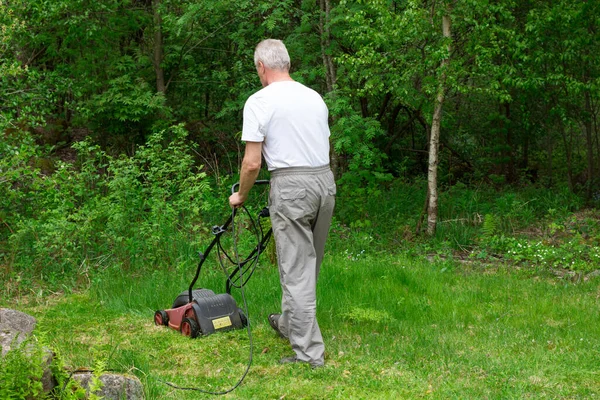 Bir adam arka bahçedeki çimleri elektrikli çim biçme makinesiyle biçiyor..