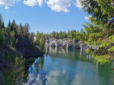 Güneşli bir yaz gününde gökyüzünün ve bulutların yansımasıyla Ruskeala Dağ Parkı 'ndaki Mermer Kanyon' un zümrüt suyunun gözlem güvertesinden görüş..