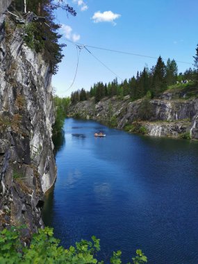 Güneşli bir yaz gününde Ruskeala Dağ Parkı 'ndaki Mermer Kanyon' un turkuaz sularında yüzen kayalıkların ve teknelerin görüntüsü.