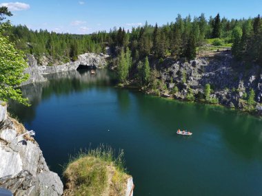 Ruskeala Dağ Parkı 'ndaki Mermer Kanyon' un turkuaz suyunun gözlem güvertesinden gökyüzünün yansıması ve güneşli bir yaz gününde ağaçların görüntüsü..