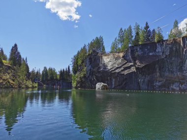 Güneşli bir yaz gününde Ruskeala Dağ Parkı 'nda turistlerin yüzdüğü Mermer Kanyon' un kayalık kıyıları ve turkuaz suları görülüyor..