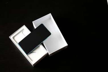 Yeni, yeni açılmış, siyah bir masada beyaz bir kutuda cep telefonunun üst görüntüsü..