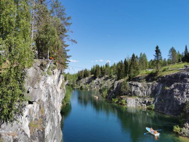 Ruskeala Dağ Parkı 'ndaki Mermer Kanyon' un turkuaz suyunun gözlem güvertesinden gökyüzünün yansıması ve güneşli bir yaz gününde ağaçların görüntüsü..