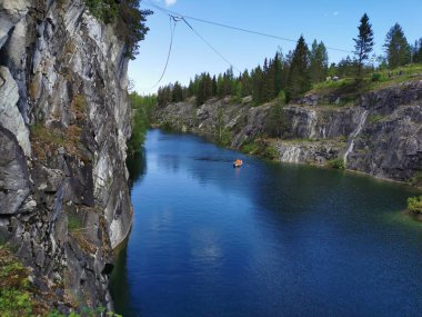 Güneşli bir yaz gününde Ruskeala Dağ Parkı 'ndaki Mermer Kanyon' un turkuaz sularında yüzen kayalıkların ve teknelerin görüntüsü.