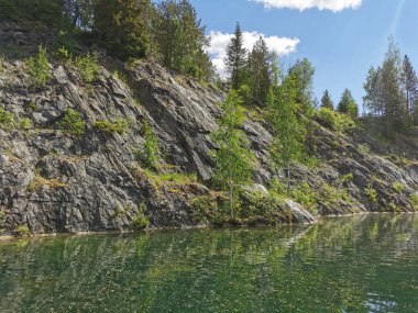Güneşli bir yaz gününde Ruskeala Dağ Parkı 'ndaki Mermer Kanyon' un kayalık kıyıları ve zümrüt suyu manzarası.