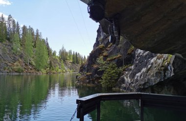Güneşli bir yaz gününde Ruskeala dağ parkında ağaçların yetiştiği su basmış Mermer Kanyon 'un dik yamacındaki yüzen platformdan manzarayı izleyin..