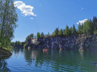 Güneşli bir yaz gününde Ruskeala Dağ Parkı 'nda turistlerin yüzdüğü Mermer Kanyon' un kayalık kıyıları ve turkuaz suları görülüyor..