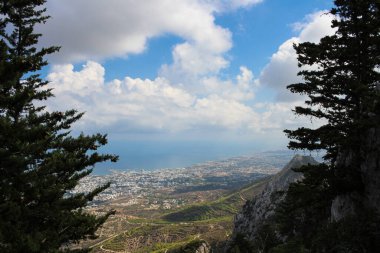 Kyrenia şehrindeki ağaçların dalları, dağlar, gökyüzü ve Akdeniz arasındaki Aziz Hilarion şatosundan panoramik manzara. Kıbrıs.