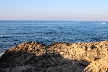 Keskin taşlar ve yüzyıllardır donmuş lavlardan oluşan deniz kıyısı, deniz ve mavi gökyüzünün arka planına karşı. Ayia Napa. Kıbrıs.