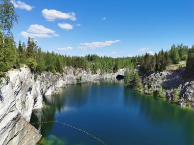 Ruskeala Dağ Parkı 'ndaki Mermer Kanyon' un turkuaz suyunun gözlem güvertesinden gökyüzünün yansıması ve güneşli bir yaz gününde ağaçların görüntüsü..