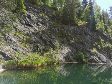 Güneşli bir yaz gününde Ruskeala dağ parkında ağaçların büyüdüğü su basmış Mermer Kanyon 'un yamacına bakın..