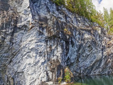 Güneşli bir yaz gününde Ruskeala Dağ Parkı 'ndaki su basmış Mermer Kanyon' un dik yamacındaki sudan manzara.