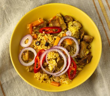 Soğan halkaları ve kırmızı acı biberli peçeteli sarı bir çaydanlıkta Asya pilavı..