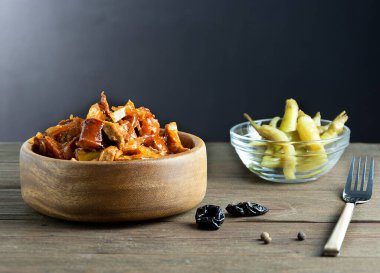 Geleneksel Polonya lahanası ve et bigosu yemeği. Ahşap bir tabakta, acı biberler, kuru erik ve çatal, ahşap bir arka planda.