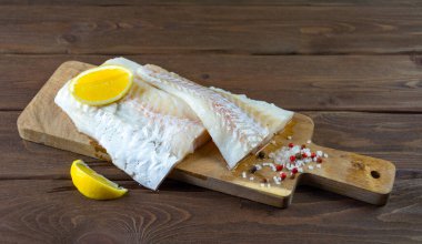 Biber, tuz ve limonla tahta bir tahtanın üzerinde morina balığı. Koyu tahta arkaplan.