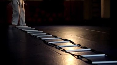 Spor salonunda beyaz kimonolu bir adam antrenman sırasında ayak egzersizi yapıyor..