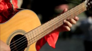 Kırmızı tişörtlü bir müzisyen açık havada gitar çalar..