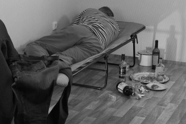 Sarhoş bir adam karyolada yatıyor ve yakınlarda boş bir içki şişesi var..