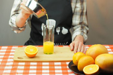 Genç bir adam şeffaf bir bardağa taze sıkılmış narenciye suyu döker..