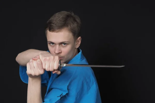 Retrato de un joven en un kimono azul con una espada. Fondo negro. —  Fotos de Stock