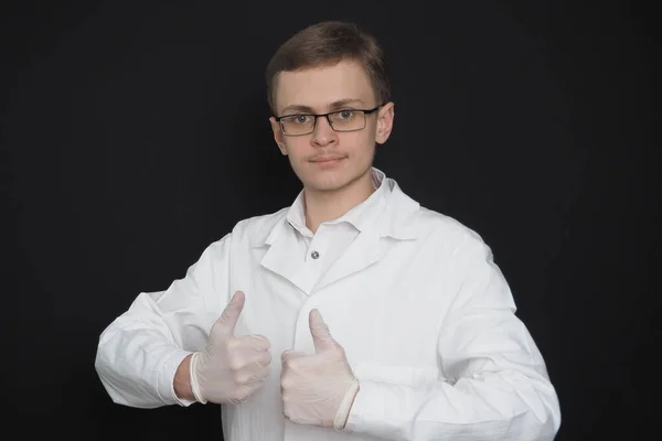 Porträt eines jungen Mannes, eines Arztes europäischen Aussehens in einem weißen medizinischen Gewand auf schwarzem Hintergrund. Ein Medizinstudent. — Stockfoto