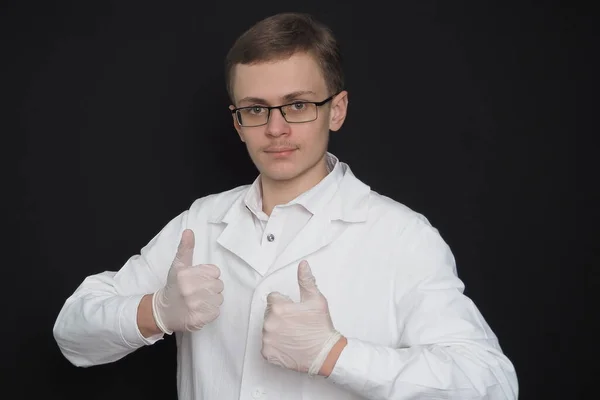 Προσωπογραφία ενός νεαρού άνδρα, ενός γιατρού ευρωπαϊκής εμφάνισης με λευκή ιατρική ρόμπα σε μαύρο φόντο. Φοιτητής ιατρικής. — Φωτογραφία Αρχείου