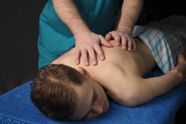 Sırt masajı iyileştiricidir. Genç bir adam masaj koltuğunda yatıyor. Erkek bir masör masaj yapar..