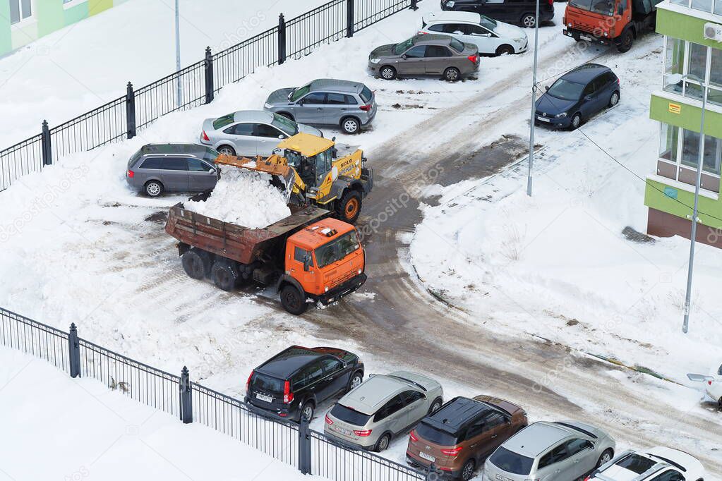 Snowplows in yards and on the streets of the city. The dump truck loads snow into the truck.