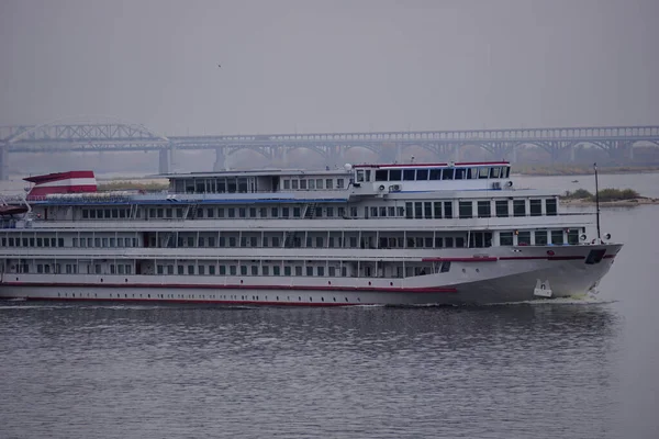 The passenger motor ship ruristic three-deck goes along the river, in the background is a large brid