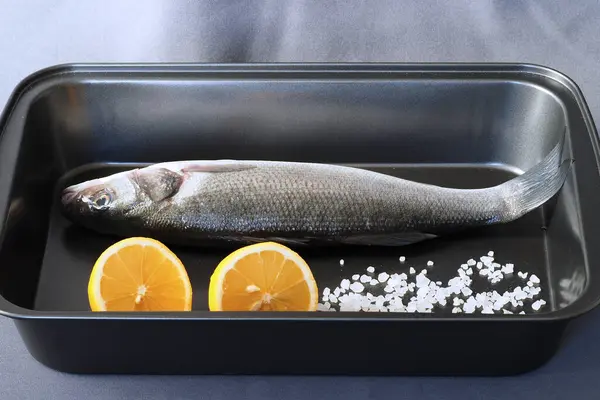 Spigola di pesce crudo fresco con limone e sale grosso su un vassoio. — Foto Stock