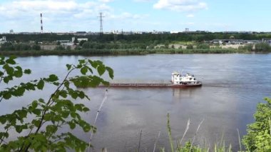 A river push boat carries a barge loaded with sand on the river in summer.