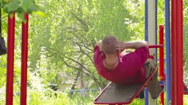 Bir adam spor için içeri girer, doğadaki bir spor sahasında karın kaslarını sallar..