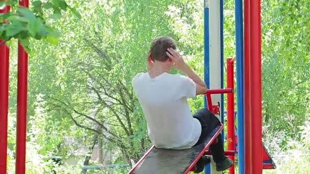 Exercício ao ar livre. Um jovem agita os abdominais no simulador. — Vídeo de Stock