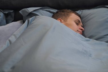 Genç adam yorganın altında yatakta uyur. Rahat ve rahat bir uyku ortamı. Yatay fotoğraf. Yüksek kalite fotoğraf