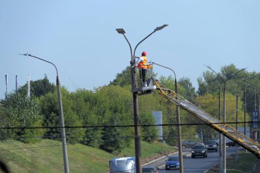 Sokak lambası. Özel elbiseli ve kask takan bir işçi sokak lambasını tamir ediyor. Yüksek kalite fotoğraf