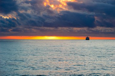 Gün batımı manzarası bulutlu güneş yansıması ve ufukta gemi var.
