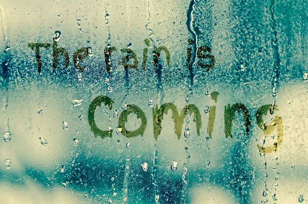 Natural water drops on glass window with word "The rain is comin — Stock Photo, Image