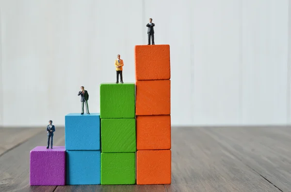 Miniature people on stack of colorful wooden cube building block — Stock Photo, Image