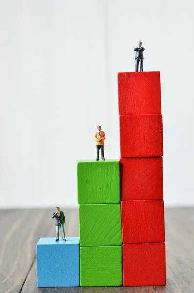 Persone in miniatura su pila di blocchi di costruzione colorati cubo di legno — Foto Stock