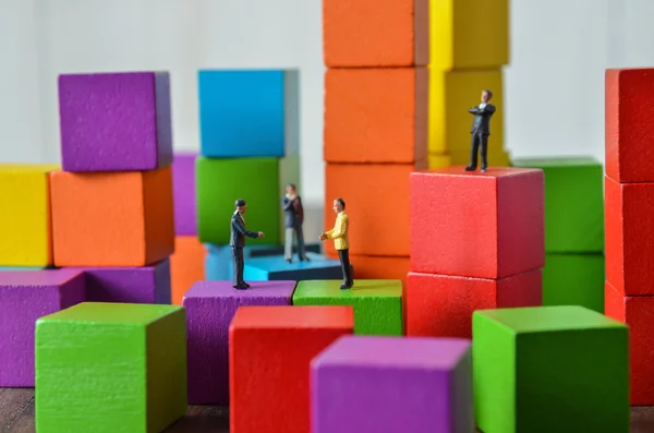 Pessoas em miniatura na pilha de bloco de construção de cubo de madeira colorido — Fotografia de Stock