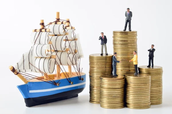 Miniatyr affärsmän på stacken av mynt och segelbåt modell — Stockfoto