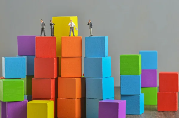 Persone in miniatura su pila di blocchi di costruzione colorati cubo di legno — Foto Stock