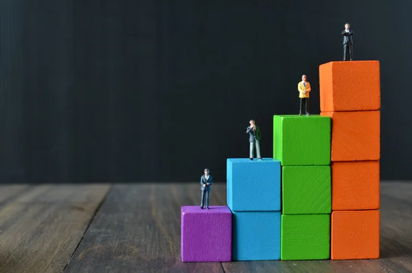 Miniature people on stack of colorful wooden cube building block — Stock Photo, Image