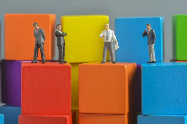 Personas en miniatura en la pila de bloques de construcción de cubos de madera de colores — Foto de Stock